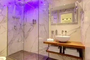 Bagno del Boutique Hotel SM Vatican Relais con doccia in vetro, lavabo su piano in legno e luci LED